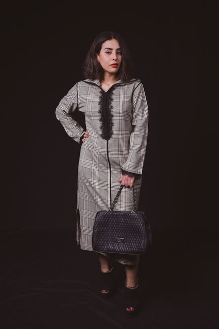 Fashionable woman in checkered dress holding a designer handbag during a studio shoot on a black background.